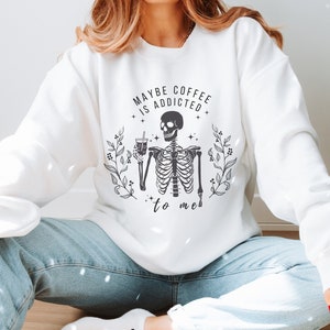 May include: White sweatshirt with a black skeleton graphic holding a coffee cup and the text "Maybe coffee is addicted to me".