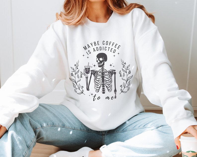 May include: White sweatshirt with a black skeleton graphic holding a coffee cup and the text "Maybe coffee is addicted to me".