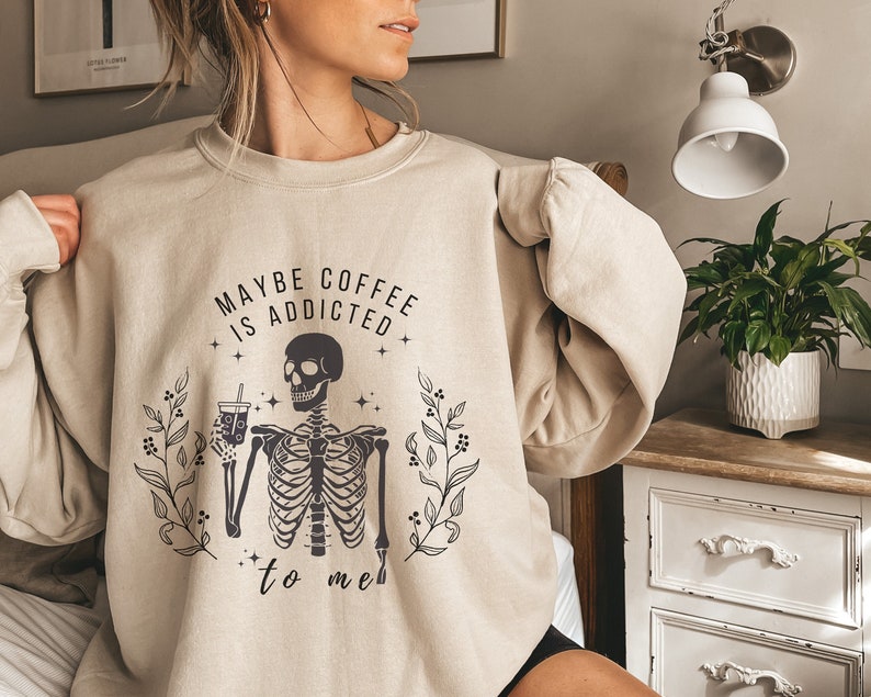 May include: A beige sweatshirt with a skeleton holding a coffee cup and the text "Maybe coffee is addicted to me".