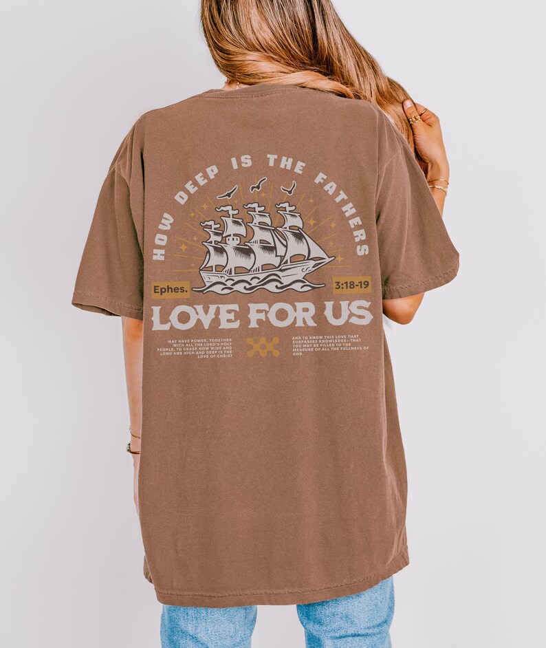 May include: A brown t-shirt with the text "HOW DEEP IS THE FATHERS LOVE FOR US" and a graphic of a ship. The text "Ephes. 3:18-19" is also printed on the shirt. The shirt is made of a soft material.