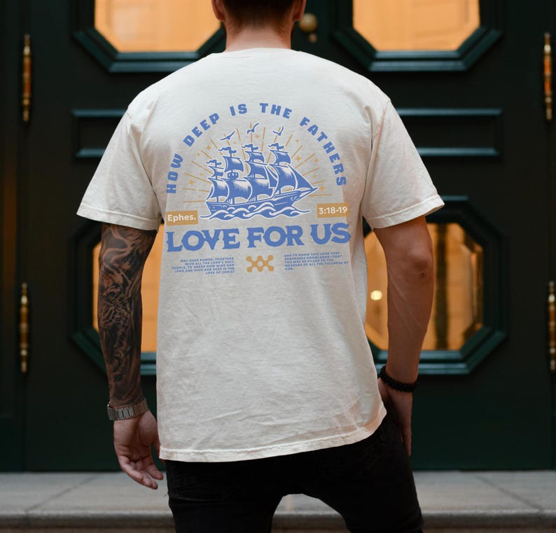 May include: Cream-colored t-shirt with a blue nautical design featuring a ship and the text "HOW DEEP IS THE FATHERS LOVE FOR US". The shirt also includes the text "Ephes. 3:18-19".