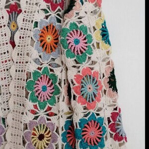 May include: A white crochet cardigan with colorful floral designs. The cardigan has long sleeves and a loose fit.