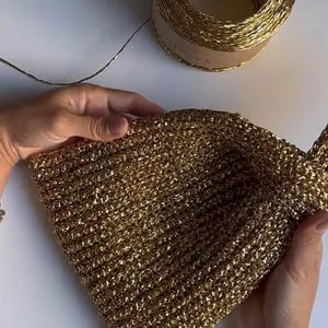 May include: A gold crocheted bag with a single strap. The bag is made of a shiny, metallic yarn.