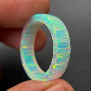 May include: A luminous opal ring, showcasing a spectrum of colors including blues, greens, and yellows. The ring's design is a solid band, with a polished, smooth surface. The opal's internal structure creates a play of light, giving it a unique, iridescent appearance.