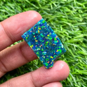 May include: A rectangular piece of blue opal with green, orange, and yellow iridescent flashes. The opal is a rough, unpolished stone.