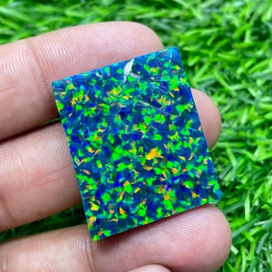 May include: A square-shaped green and blue opal gemstone with iridescent flashes of color.