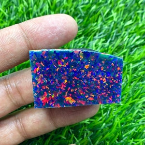 May include: A blue, green, red, and orange opal gemstone with a rough, natural finish. The opal is a rectangular shape and is approximately 2 inches long.
