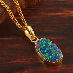Könnte beinhalten: Eine goldene Kettenkette mit einem Anhänger mit einem ovalen Opal-Edelstein in Grün, Blau und Rot.