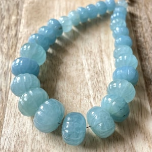 May include: A strand of light blue aquamarine beads, each bead is carved with a textured design. The beads are strung on a thin wire and are approximately 1 cm in diameter.