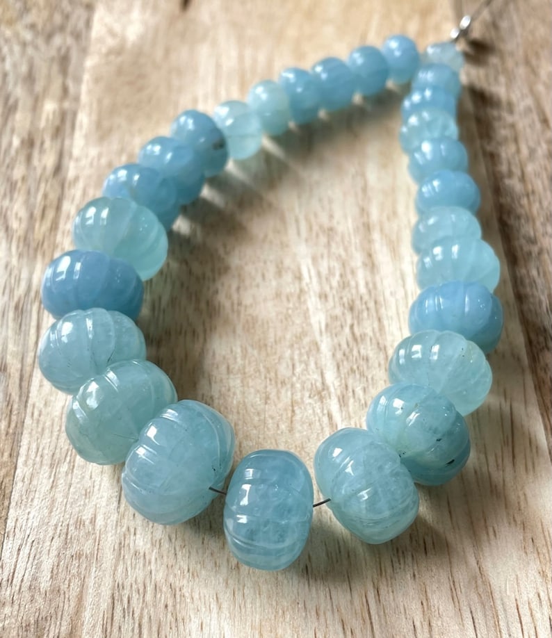 May include: A strand of light blue aquamarine beads, each bead is carved with a textured design. The beads are strung on a thin wire and are approximately 1 cm in diameter.