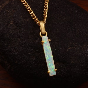May include: A gold chain necklace with a pendant featuring a white opal gemstone. The opal is a rectangular shape with a light blue and green iridescent sheen.