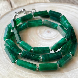 Op de afbeelding: Een groene edelsteen ketting met rechthoekige kralen en zilveren tussenstukken. De ketting ligt op een houten oppervlak.