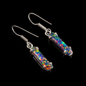 May include: A pair of silver earrings with a long, rectangular, iridescent opal stone. The stones have a black base with flashes of green, blue, red, and yellow.