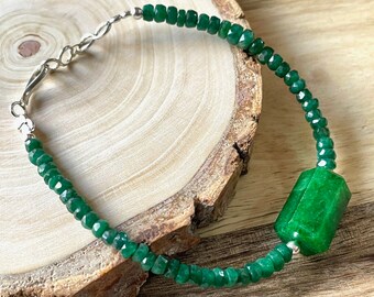 May include: A green gemstone bracelet with a large, faceted, green gemstone bead. The bracelet is made with silver-toned metal.