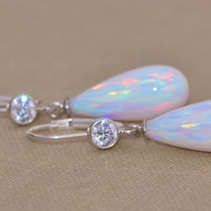May include: A pair of silver teardrop earrings with a white opal stone and a clear crystal accent.