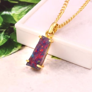 Op de afbeelding: Een gouden hangerketting met een rechthoekige opaalsteen. De opaal heeft een mix van rode, blauwe en paarse kleuren. De hanger wordt vastgehouden door een gouden zetting en hangt aan een fijne gouden ketting. De steen is ongeveer 2 cm lang.