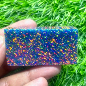 Op de afbeelding: Een blauwe, groene en oranje opaal edelsteen met een ruw, getextureerd oppervlak. De opaal is rechthoekig van vorm en ongeveer 2,5 cm lang.