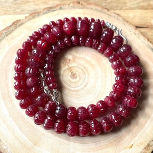 May include: A strand of deep red ruby beads, each bead is round and slightly irregular in shape. The beads are strung on a silver chain with a clasp.