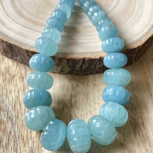May include: A strand of light blue aquamarine beads, each bead is carved with a textured design. The beads are strung on a silver thread.