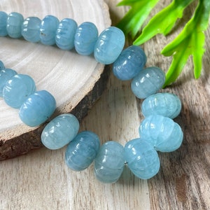 May include: A strand of light blue aquamarine beads with a faceted, carved design. The beads are strung on a clear thread and are arranged in a circular pattern.