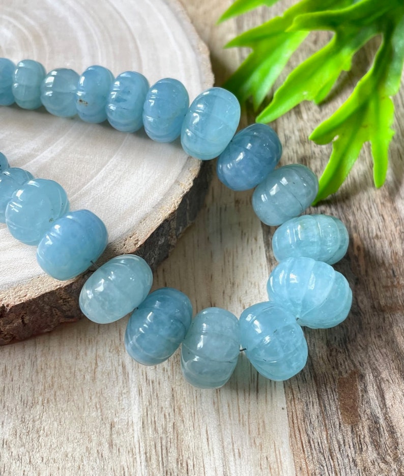 May include: A strand of light blue aquamarine beads with a faceted, carved design. The beads are strung on a clear thread and are arranged in a circular pattern.