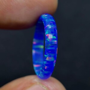 Può includere: Un anello sottile blu con intarsi di opale iridescente. L'anello è realizzato in resina e ha una finitura liscia e lucida.