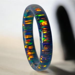 May include: A blue ring with iridescent opal flakes embedded in the resin. The ring has a smooth, polished finish.