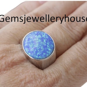 May include: A silver ring with a large blue opal gemstone. The opal has a speckled pattern of light blue and dark blue.