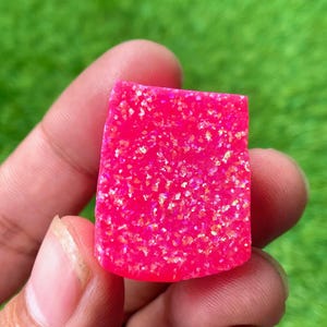 May include: A pink opal cabochon with iridescent sparkle. The stone is cut in a rectangular shape with rounded edges.