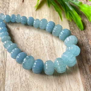 May include: A strand of light blue aquamarine beads with a carved pumpkin shape. The beads are strung on a clear elastic cord.