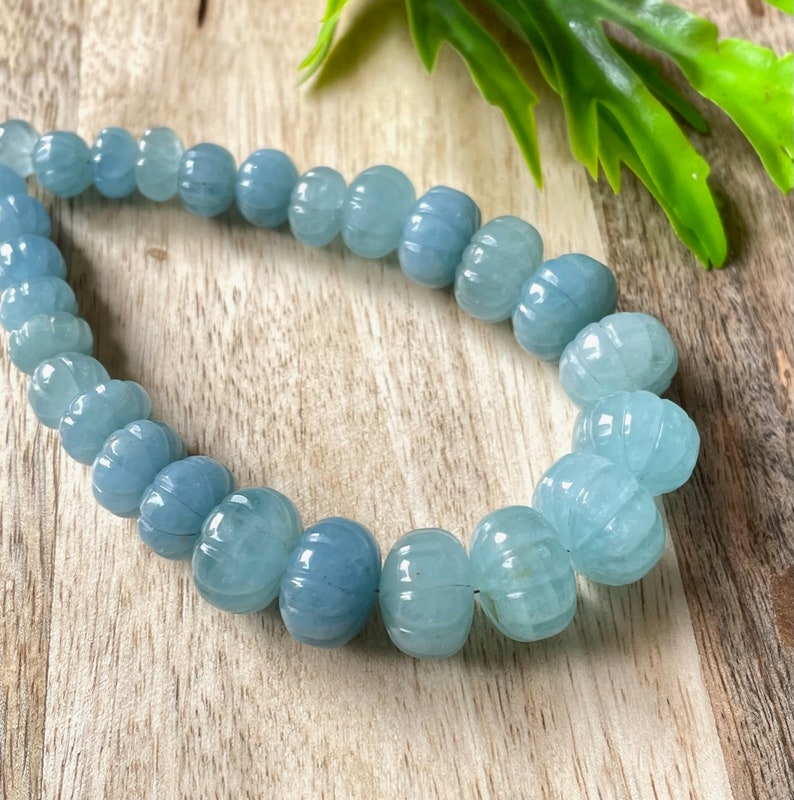 May include: A strand of light blue aquamarine beads with a carved pumpkin shape. The beads are strung on a clear elastic cord.