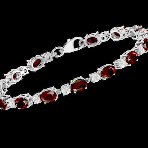 Könnte beinhalten: Ein silbernes Armband mit einem Verschlussverschluss verfügt über eine Reihe ovaler roter Edelsteine, die in Silber gefasst sind, mit kleineren klaren Edelsteinen zwischen jedem roten Edelstein.