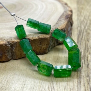 May include: A strand of green gemstone beads, each bead is a rectangular prism with a faceted finish. The beads are strung on a silver wire.