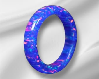 May include: A blue opal ring with iridescent shimmer and pink accents. The ring is made of a smooth, polished material and has a simple, elegant design.