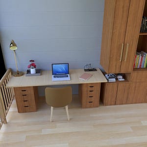 May include: A modern home office setup featuring a light wood desk with drawers, a laptop, and a tan chair. A built-in wooden cabinet provides storage. A gold desk lamp and a small floral arrangement add decorative touches. The room has a large window.