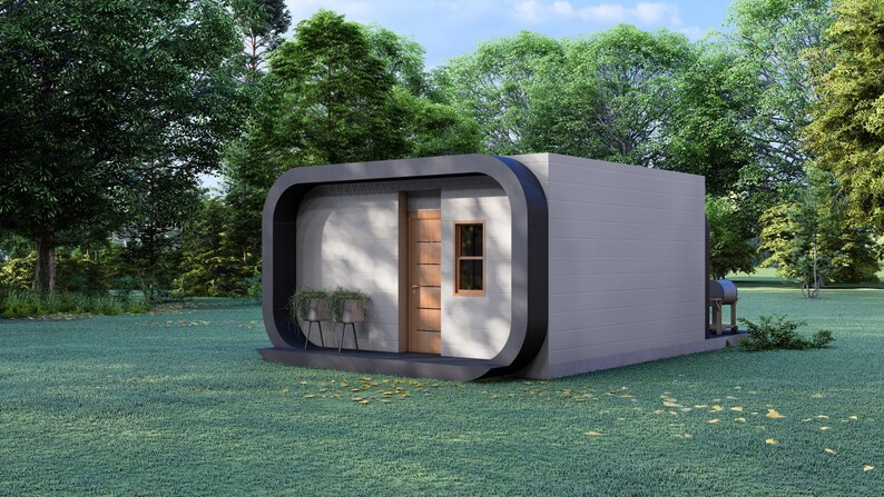 May include: A modern, gray, rectangular structure with a curved black frame around the entrance. The building has a wooden door, a small window, and a small porch with potted plants. The structure is set on a green lawn with trees in the background.