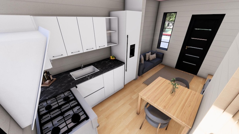 Puede incluir: Vista interior de una cocina y comedor modernos. Los armarios y electrodom&eacute;sticos blancos contrastan con una encimera negra. Una mesa y sillas de madera est&aacute;n en primer plano, con un sof&aacute; peque&ntilde;o y una ventana en el fondo.