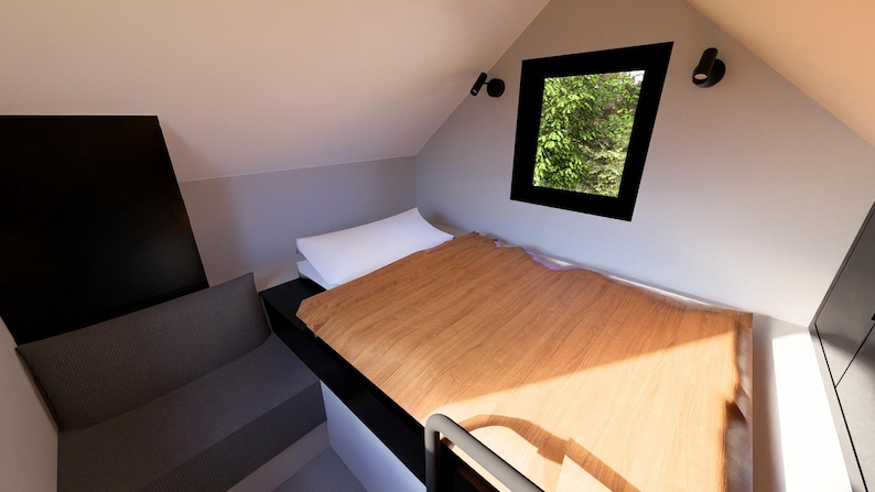 以下が含まれることがあります： ベッドと作り付けのソファを備えた、小さくモダンな寝室のインテリア。ベッドには木製のヘッドボードと白い枕があります。黒いフレームの窓からは緑の葉が見えます。部屋はニュートラルな色調で塗装されています。