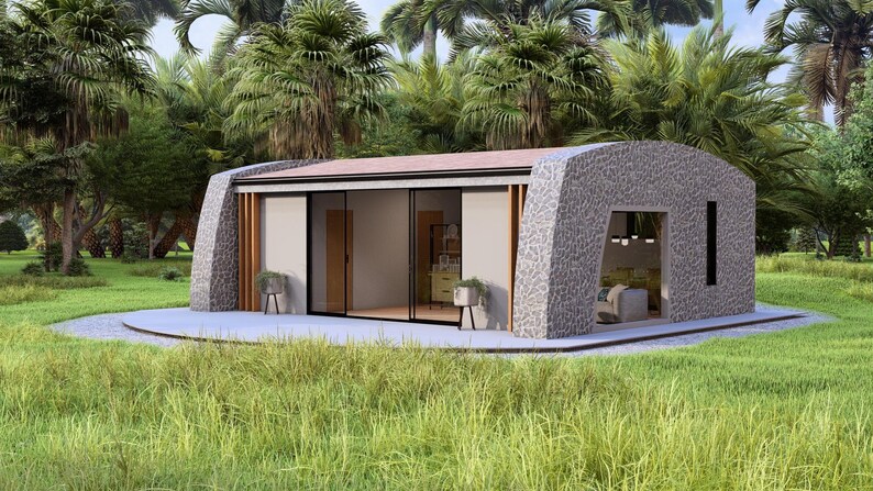May include: A modern, stone-clad house with a curved roof and large glass sliding doors. The home is surrounded by lush greenery, including palm trees and grass. The interior is visible through the glass, showcasing a minimalist design.