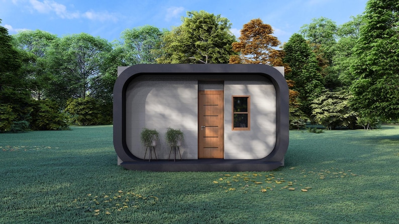May include: A modern, minimalist cabin with a dark gray rounded frame. The cabin has a wooden door, a small window, and two potted plants. The structure is set on a grassy lawn, surrounded by trees under a blue sky.