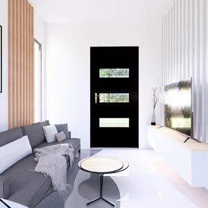 Op de afbeelding: Een moderne woonkamer met een grijze bank, een zwarte deur met rechthoekige ramen en een ronde salontafel. Een groot ingelijst kunstwerk hangt aan de muur. De kamer heeft witte muren en een lichtgekleurde vloer.