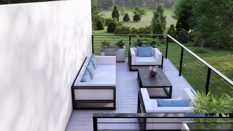 May include: Modern outdoor patio furniture set. The set features a white sofa, two armchairs, and a coffee table with black frames. Light blue cushions and pillows provide colour. The patio has a wooden deck and a black railing, with a garden view.