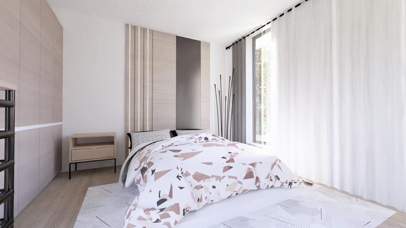 Op de afbeelding: Een modern slaapkamerinterieur met een bed met een patroon dekbed in wit, bruin en grijstinten. De kamer heeft een houten hoofdbord, een nachtkastje en een groot raam met witte gordijnen. De muren zijn wit geschilderd.