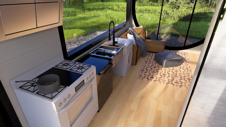 May include: Interior view of a tiny home kitchen with a white stove, a sink, and a black faucet. A gray pot sits on the stove. The kitchen has a large window with a view of green grass and trees. A small rug and seating area are visible.