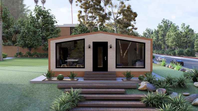 Puede incluir: Una casa moderna de una sola planta con fachada beige, ventanas con marcos negros y una puerta oscura. La casa tiene un tejado inclinado y est&aacute; rodeada de vegetaci&oacute;n, incluyendo hierba, &aacute;rboles y arbustos. Unas escaleras de madera conducen a la entrada.