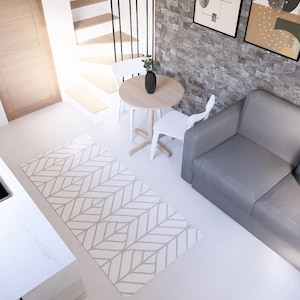 May include: Interior view of a compact living space with a kitchen area. A grey sofa with cushions is against a stone wall. A small round table and two white chairs are near a patterned rug. A hob and sink are visible.