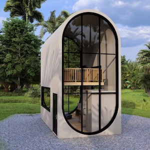 May include: A modern, two-story tiny house with a unique oval window design. The structure features a light-colored exterior, large glass windows, and a small balcony. The house is surrounded by lush green trees and grass, with a gravel path leading up to it.