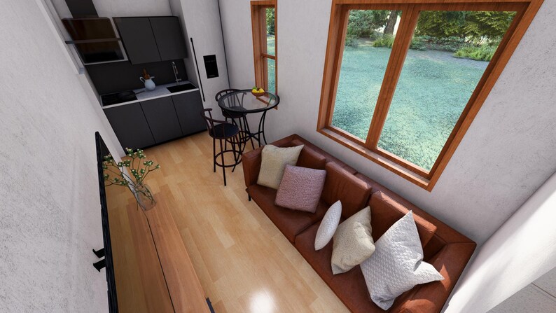 May include: Interior shot of a modern tiny home. Features include a brown leather sofa with decorative pillows, a small kitchen with dark gray cabinets, and a dining area with a round table and stools. Large windows offer a view of the outdoors.