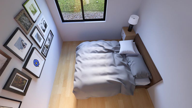 Puede incluir: Una escena de dormitorio con una cama con ropa de cama gris, una almohada blanca y una cabecera de madera. Una peque&ntilde;a mesita de noche con una l&aacute;mpara est&aacute; al lado de la cama. Una colecci&oacute;n de cuadros enmarcados cuelga de la pared. Se ve una ventana.