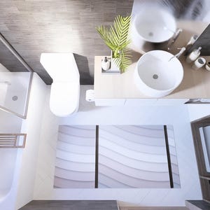 Op de afbeelding: Een bovenaanzicht van een moderne badkamer met witte armaturen en een neutraal kleurenpalet. De kamer omvat een toilet, een douche, een dubbele wastafel en een wasmachine. Een decoratief tapijt met een golfpatroon.